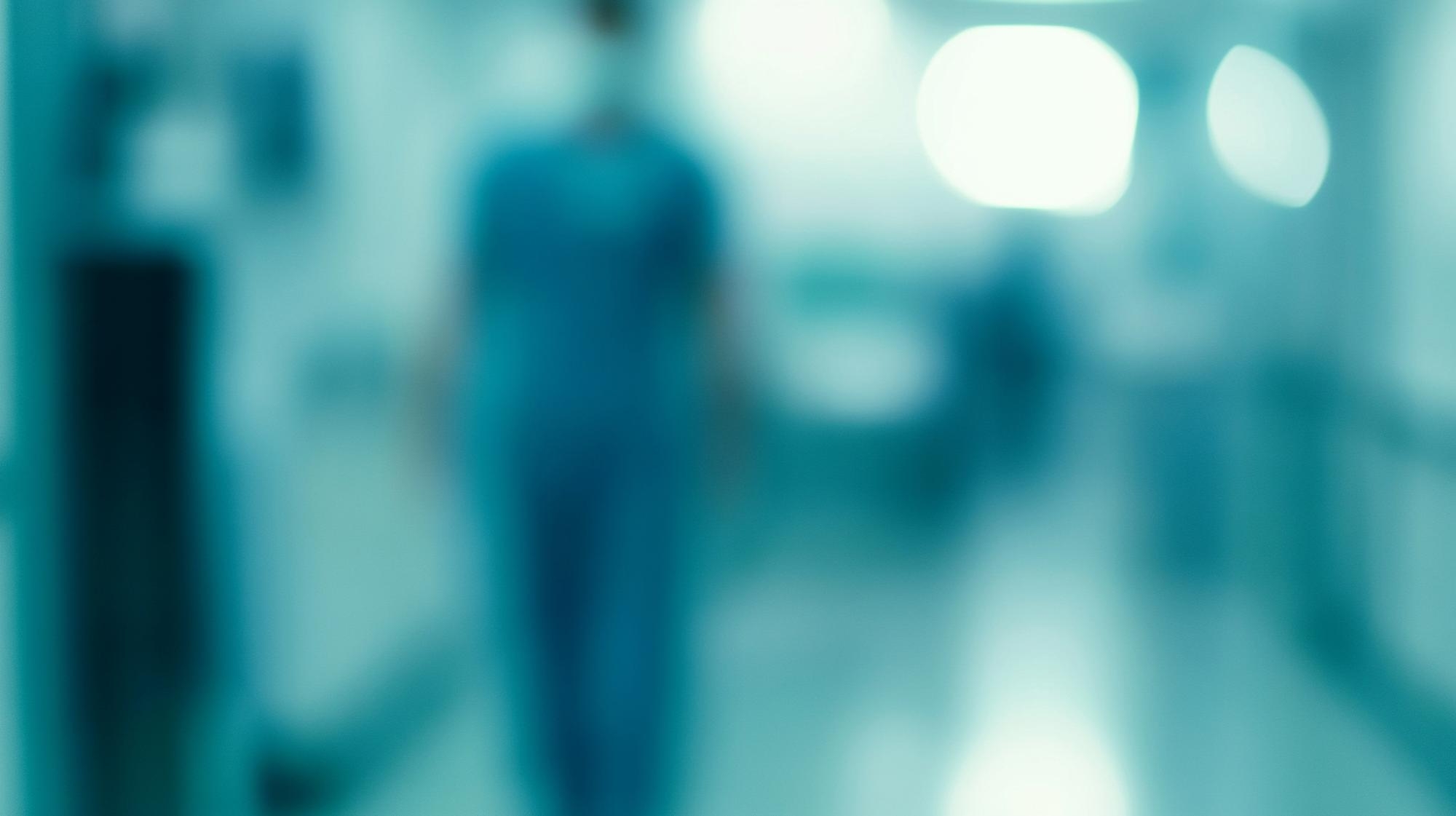 Ezra Mega Case Study 1 Blurred figure standing in a hospital corridor with bright lights and a blue-toned background.