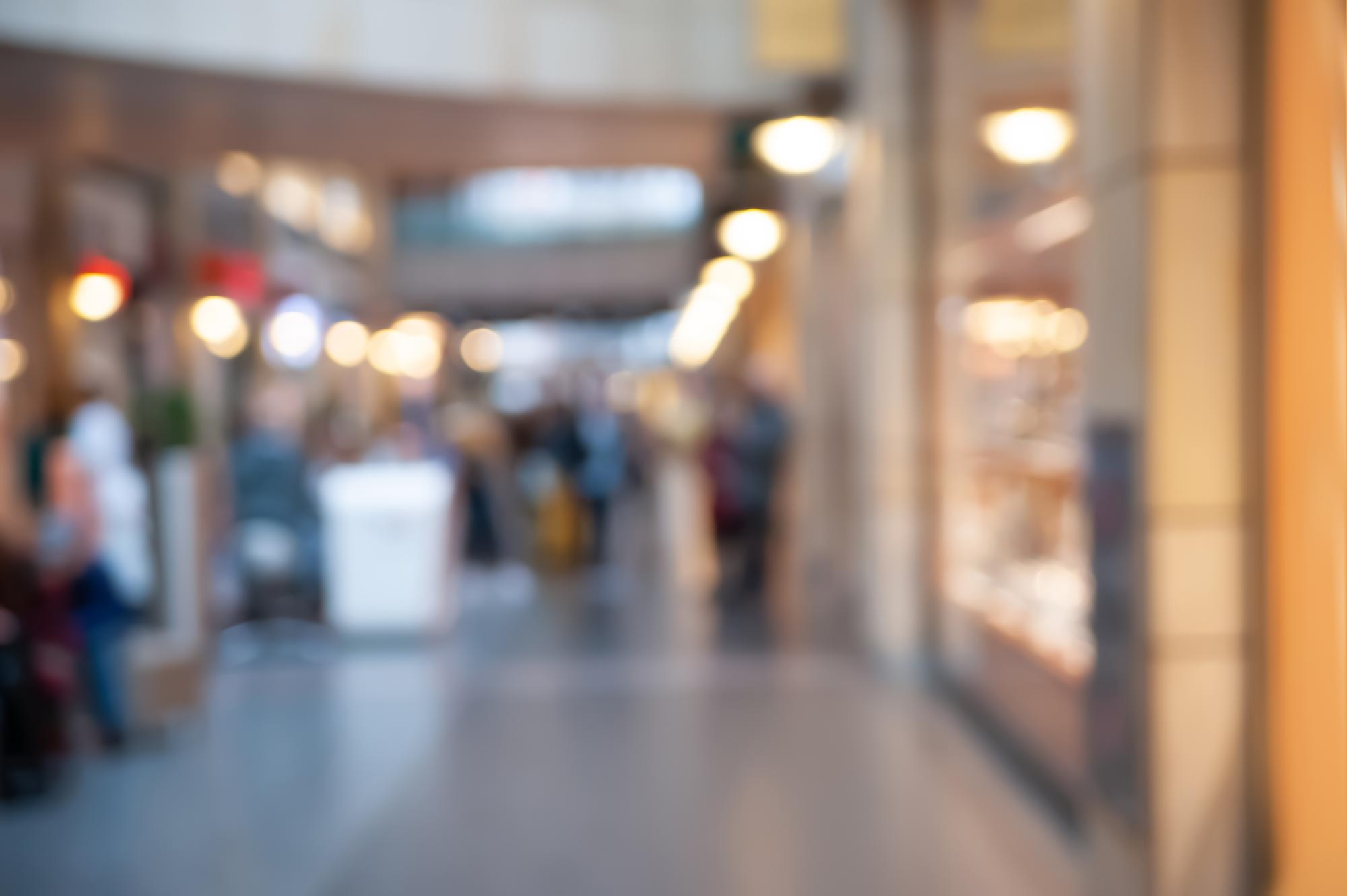 Assosia 4 Blurred retail checkout counter with a cashier in the background and products on the counter in the foreground.