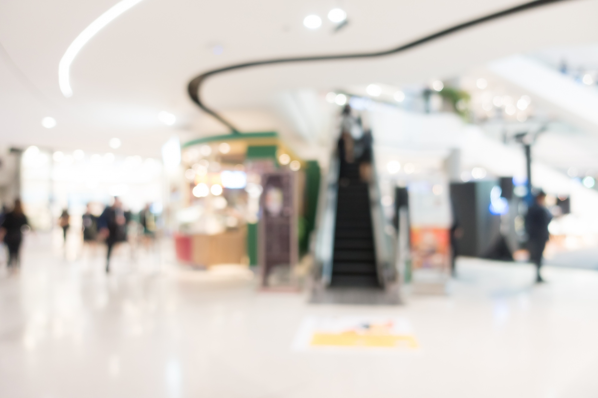 Assosia 2 Blurred view of a multi-level shopping mall atrium with curved balconies and storefront lights in the background.