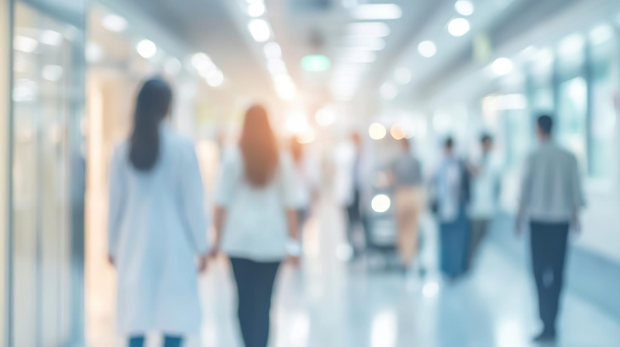 Hammersmith Medicines Research 3 Soft-focus view of doctors and staff walking through a bright hospital hallway.